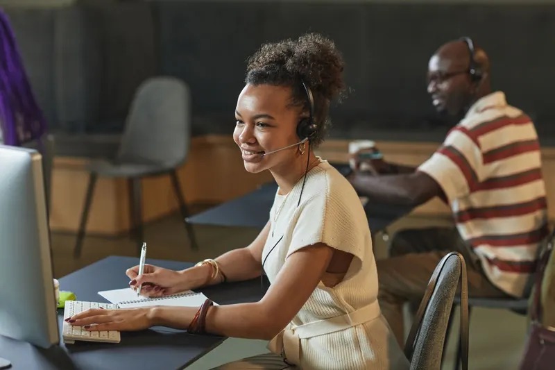 Atendente sorrindo com headset enquanto anota um pedido